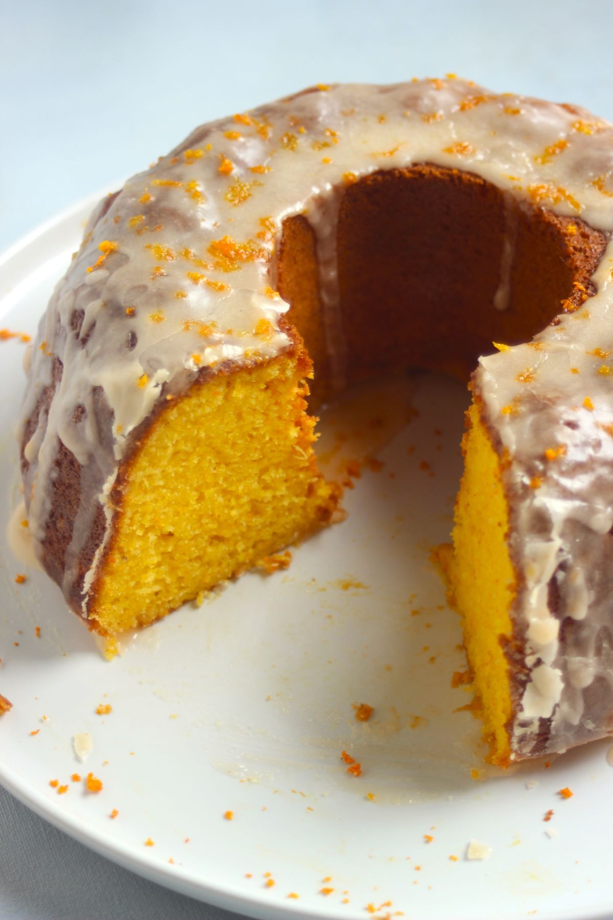 Gluten-free mandarin bundt cake, without a piece, and topped with icing on a white plate.