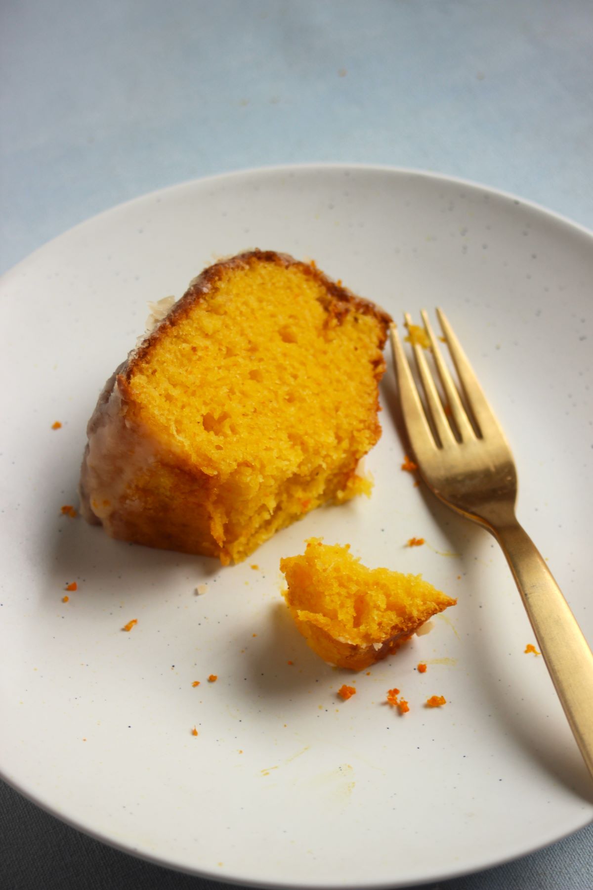 A piece of mandarin cake on a white plate and a golden fork.