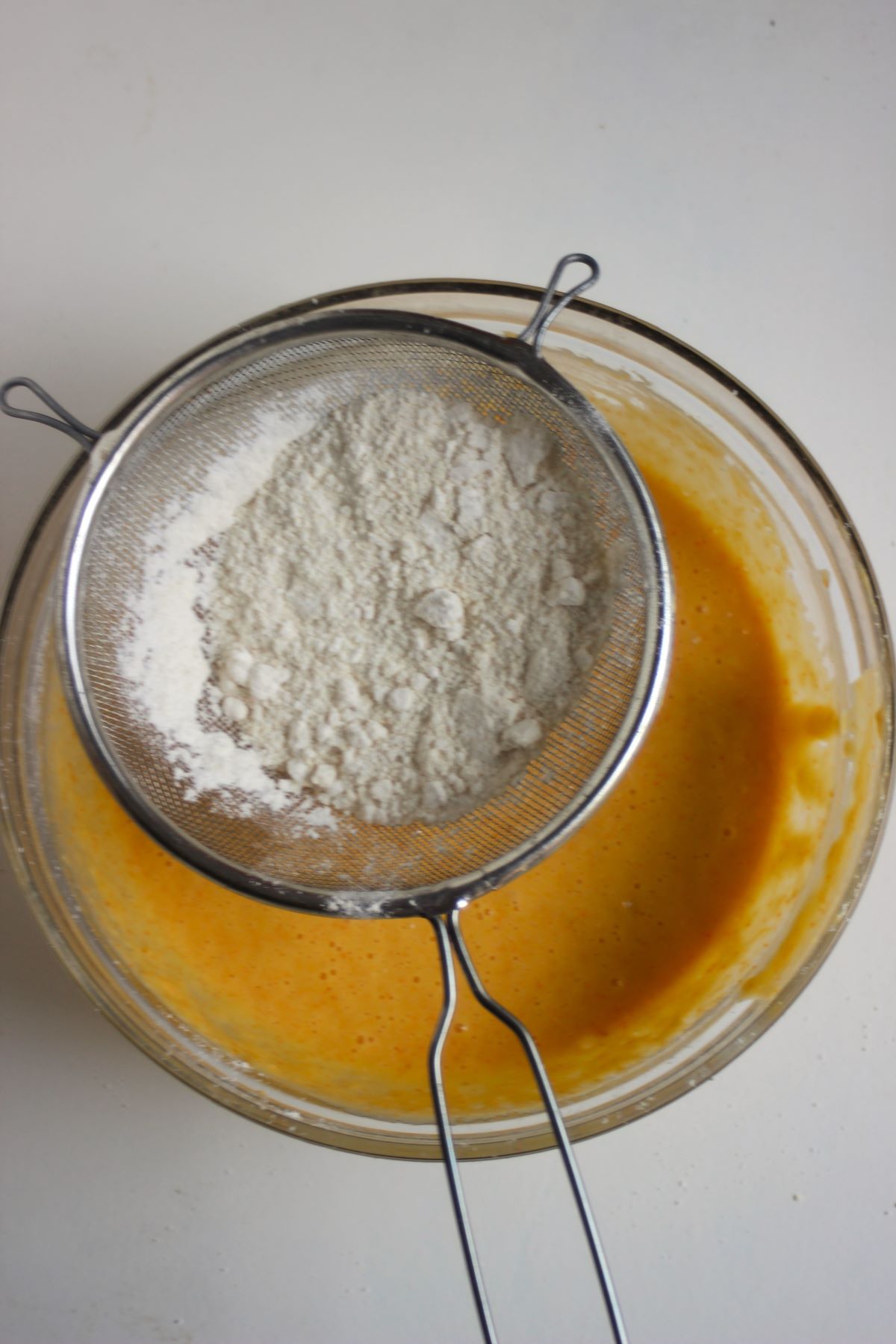 A strainer with flour to be sift into the glass bowl with an orange,