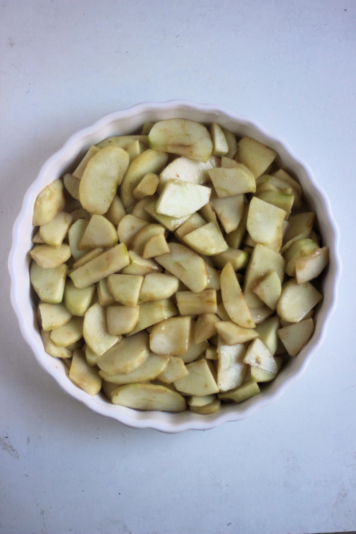 Round baking pan with sliced apples on a white surface seen from above.