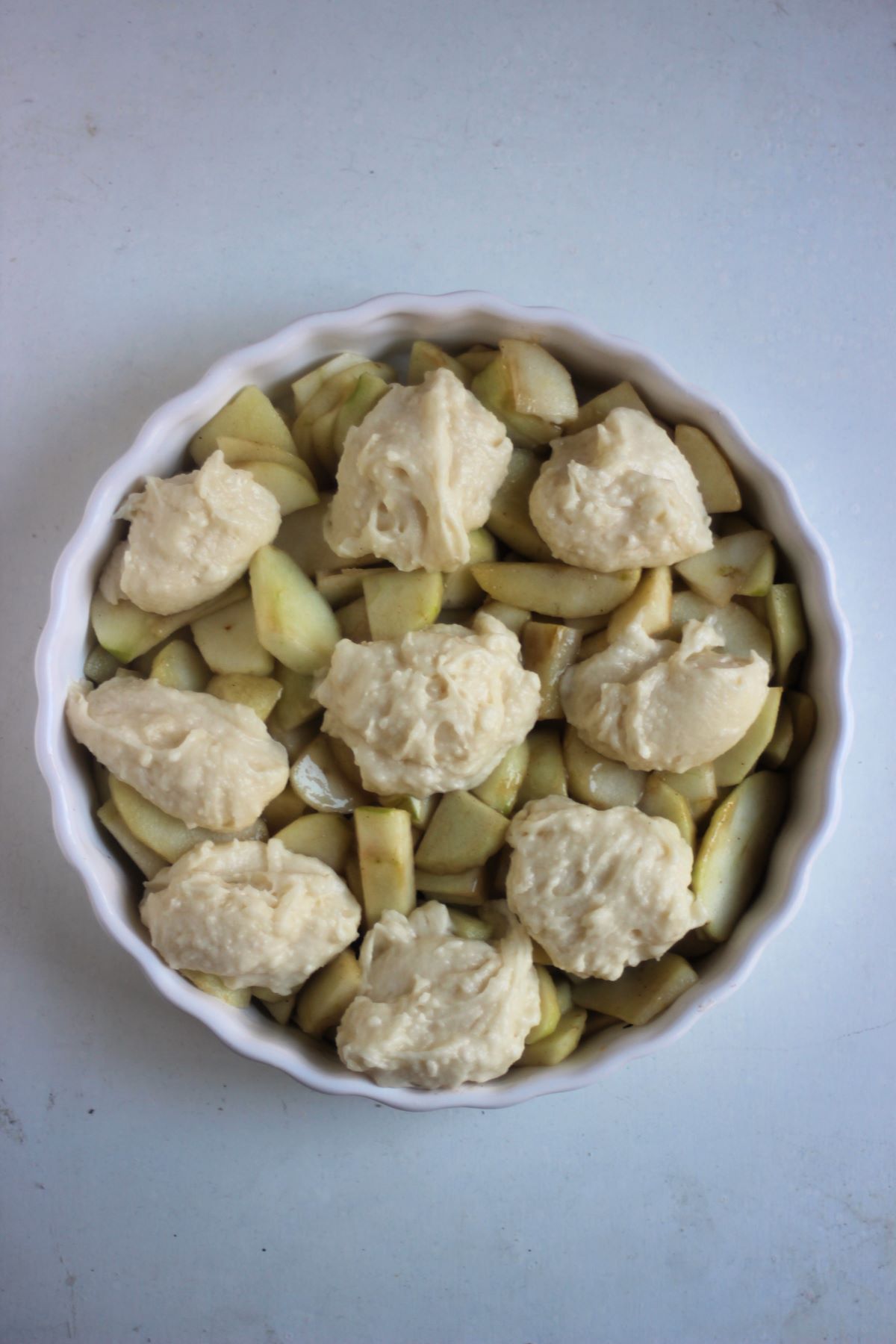 Round baking pan with sliced apples and batter balls seen from above.