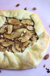 Apple galette on a pink surface. Almonds on the side.