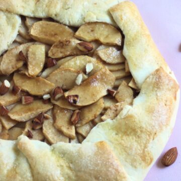 Apple galette on a pink surface. Almonds on the side.