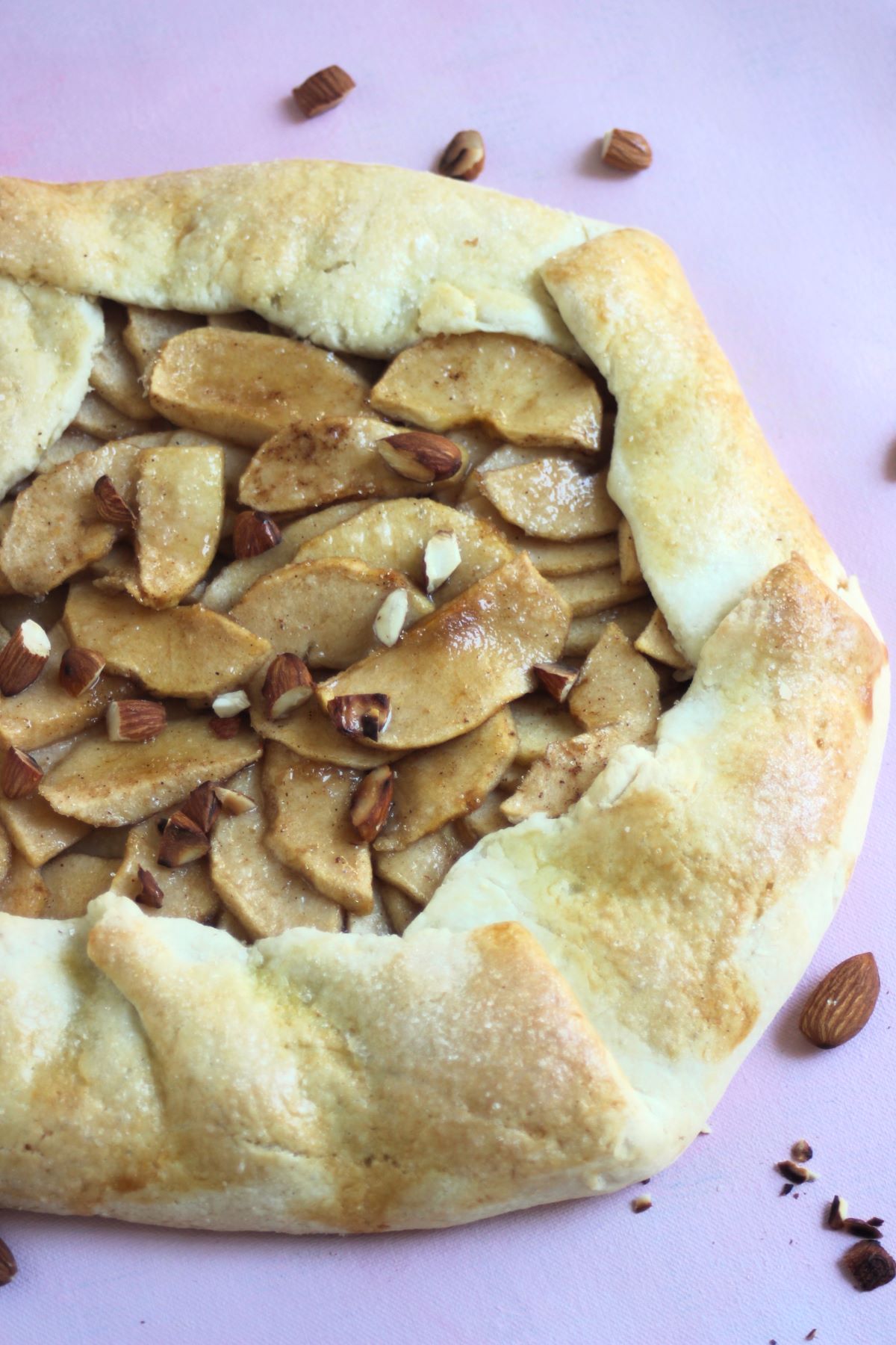 Apple galette on a pink surface. Almonds on the side.