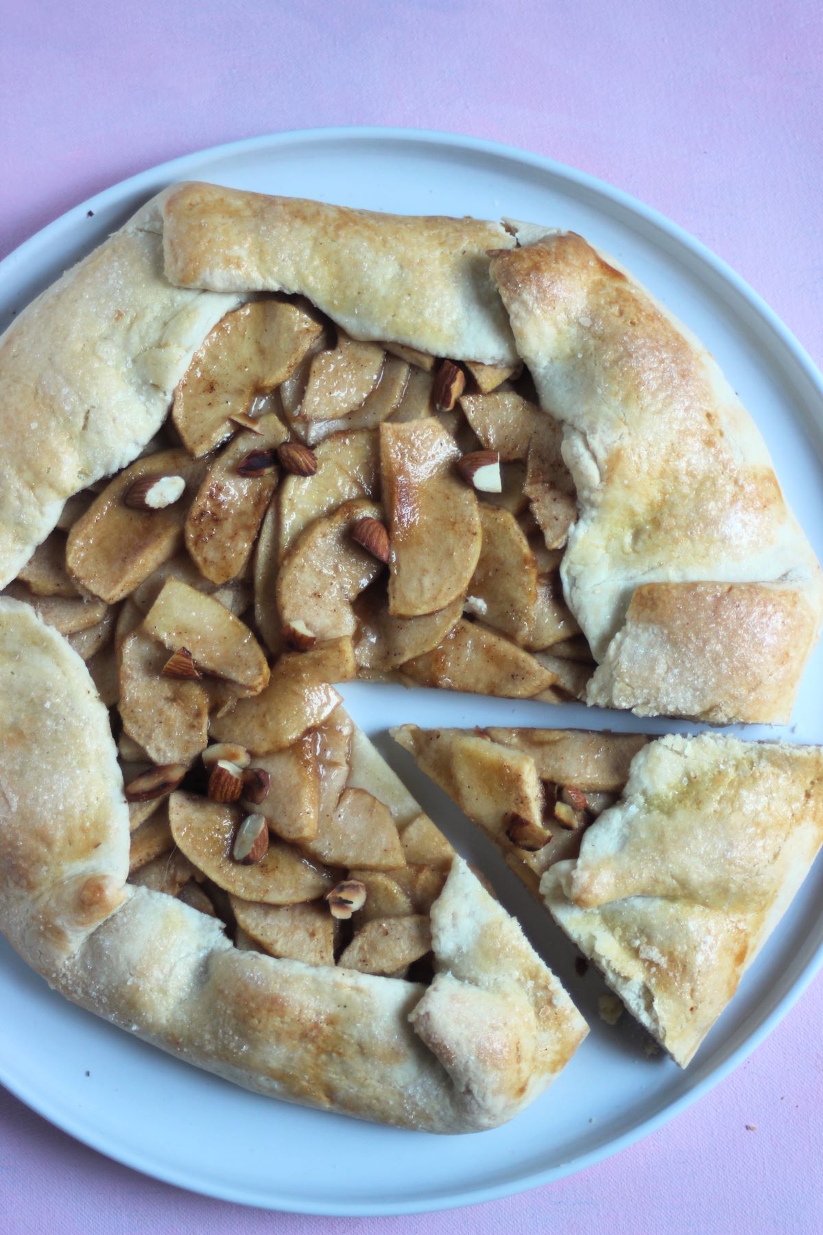 Apple galette with a portion cut on a white plate on a pink surface seen from above.