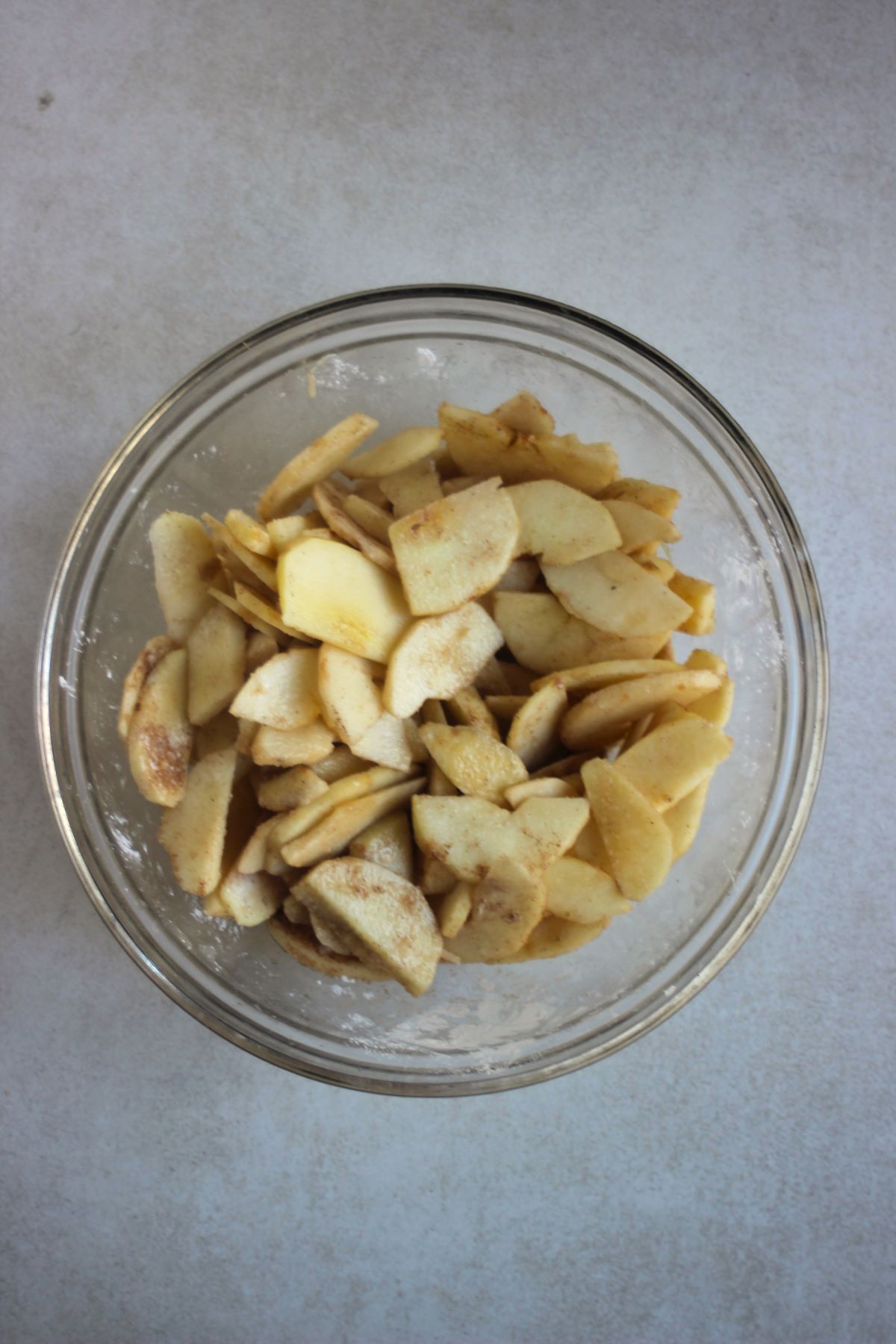 Glass bowl with peeled and sliced apples with brown sugar and cornstarch.