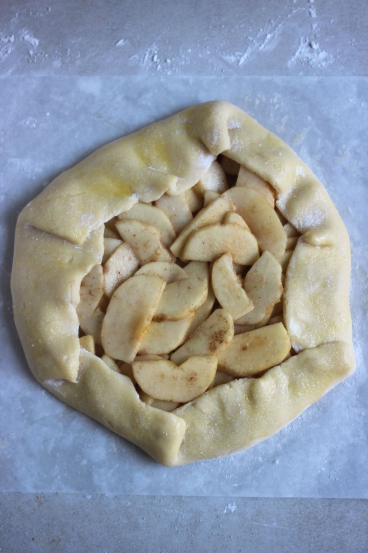 Raw apple galette on a parchment paper.