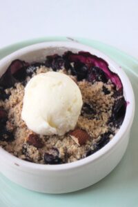 Blueberry crisp with a scoop of vanilla ice cream on an aqua green plate.