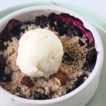 Blueberry crisp with a scoop of vanilla ice cream on an aqua green plate.