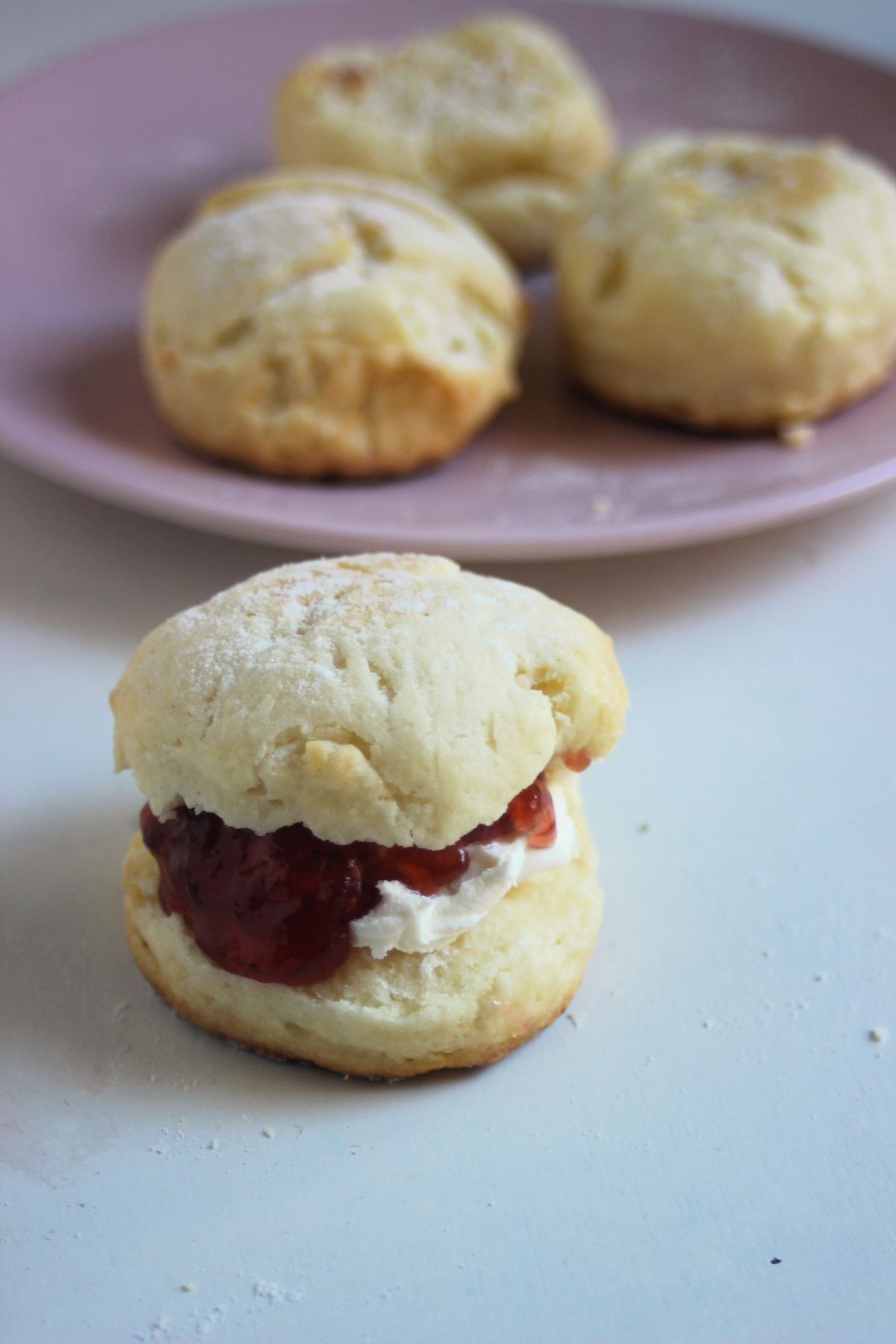 Scon filled with cream cheese and jam. More scons behind on a pink plate.