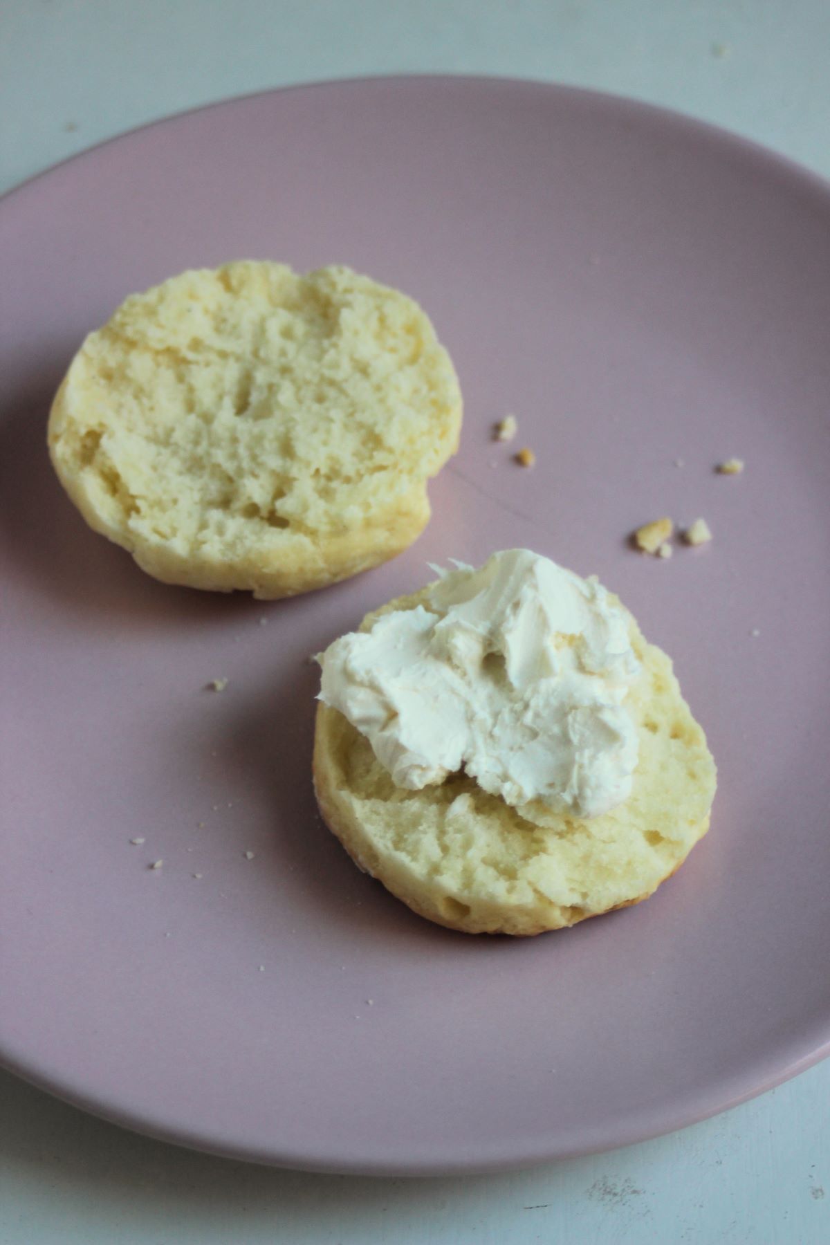 A scon cut in two half on a pink plate. One is topped with cream cheese.