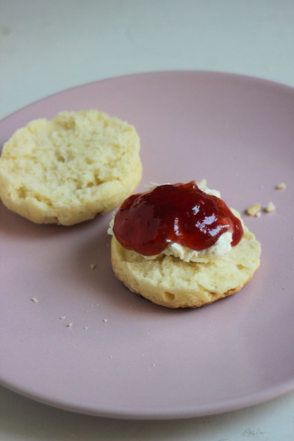 Scon cut in two half on a pink plate. One is topped with cream cheese and jam