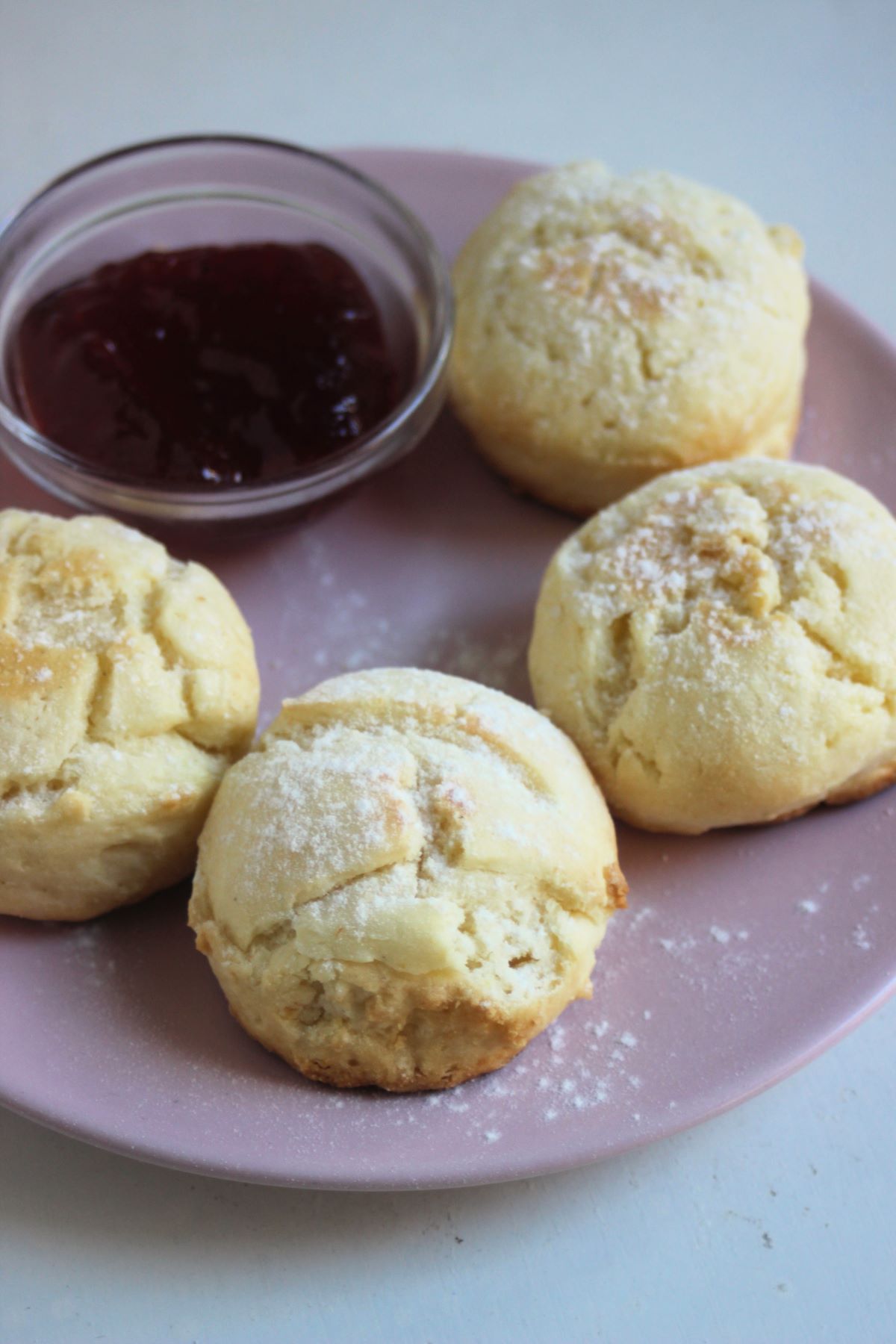 Four scons on a pink plate with a dip of jam.