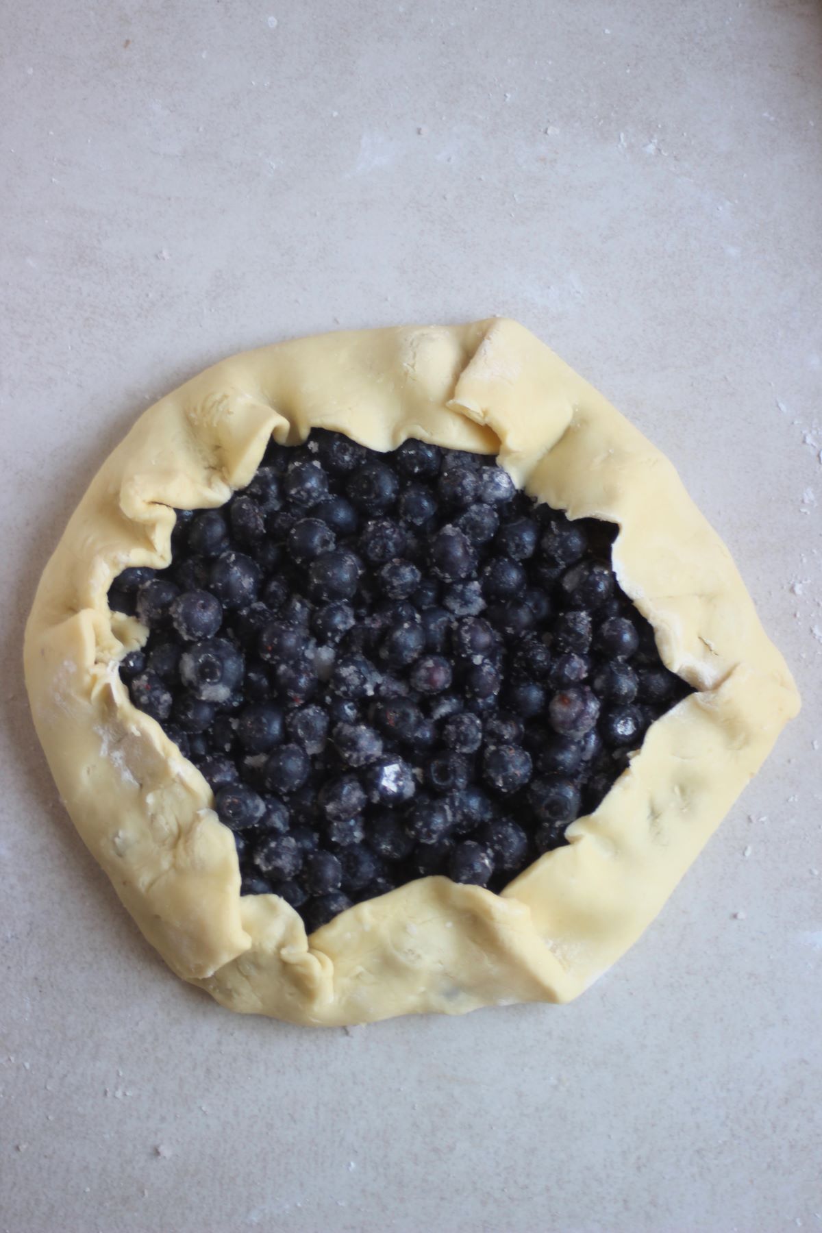 Raw blueberry galette on a white surface seen from above.