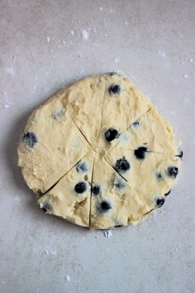 A flat circle dough with blueberries on a conter cut in triangles.