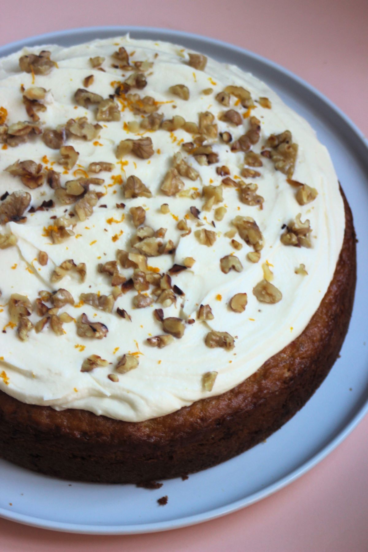 Carrot cake with cream cheese frosting and chopped walnuts on a white plate.