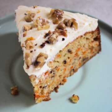 Portion of carrot cake with cream cheese frosting and chopped walnuts on an aqua green plate.