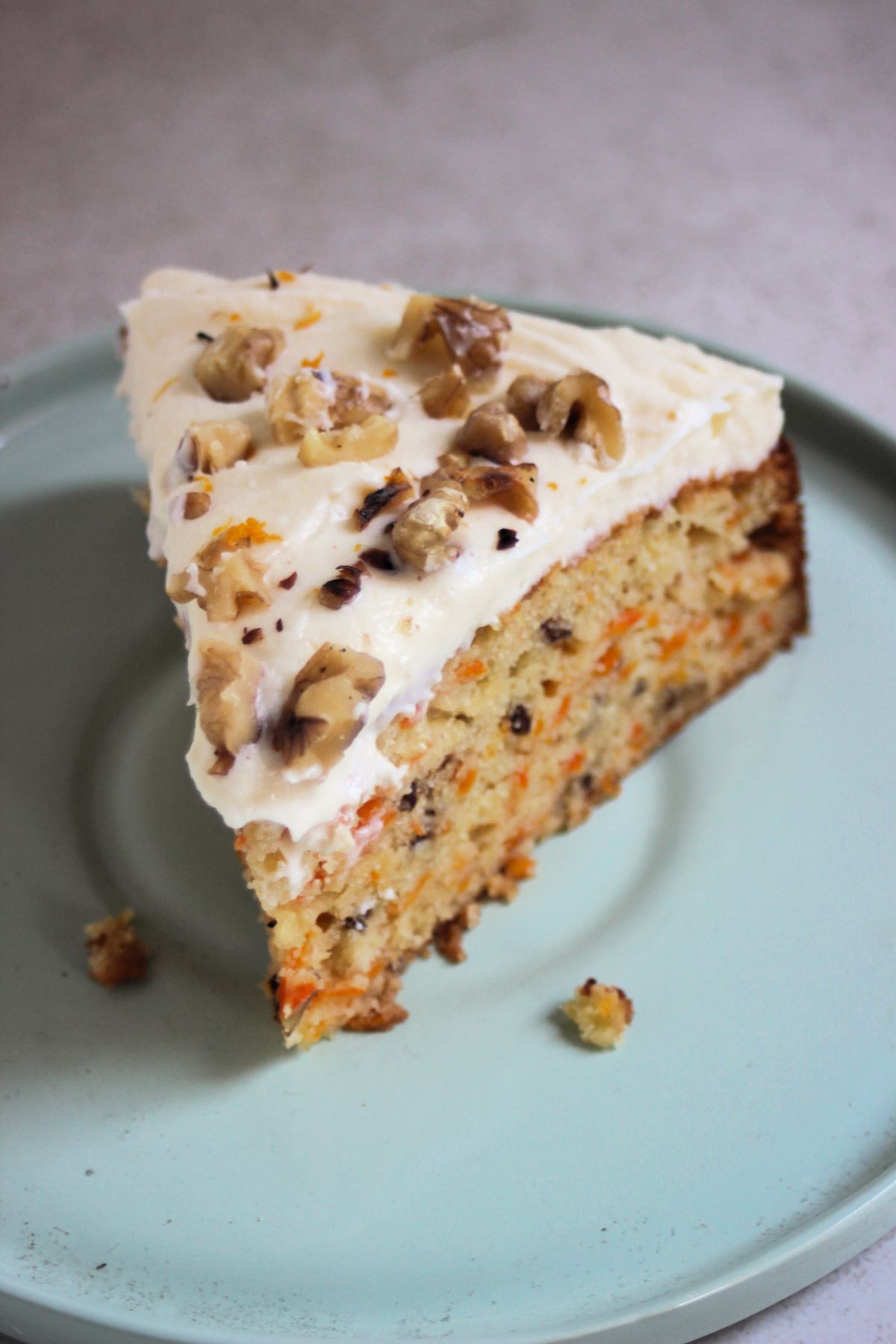 Portion of carrot cake with cream cheese frosting and chopped walnuts on an aqua green plate.