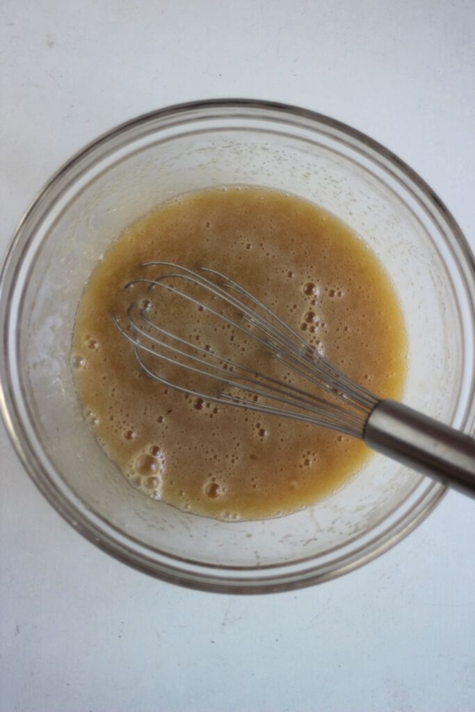 Glass bowl with a brown liquid and a hand mixer.