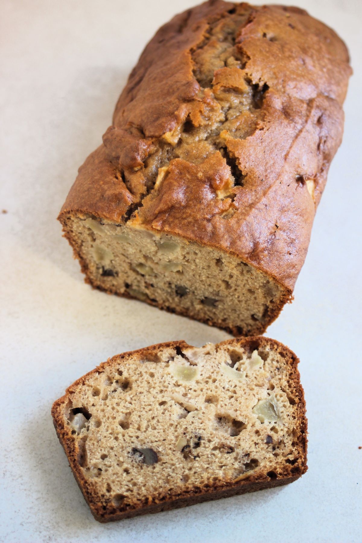 Apple bread and a slice of it on a white surface.