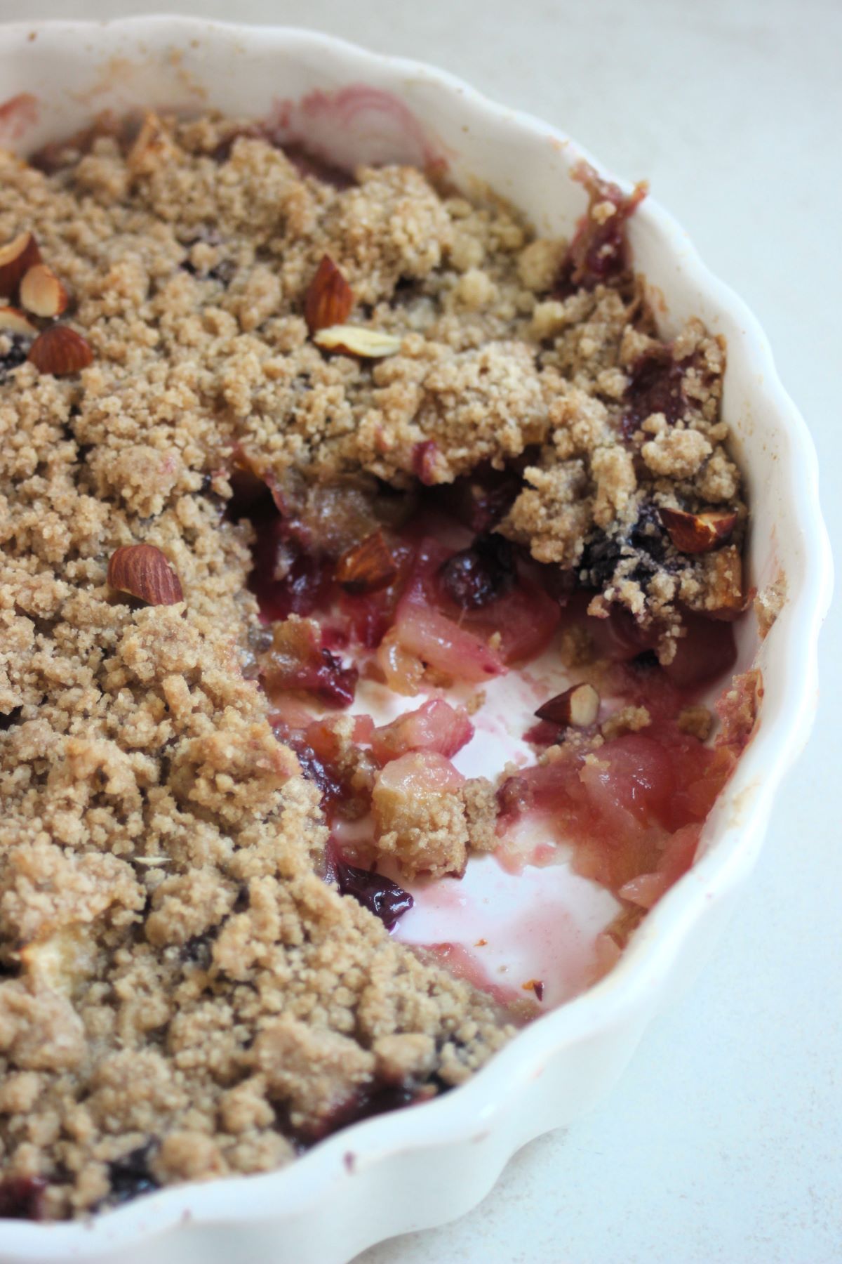 Apple crumble without a piece in a round white baking dish.