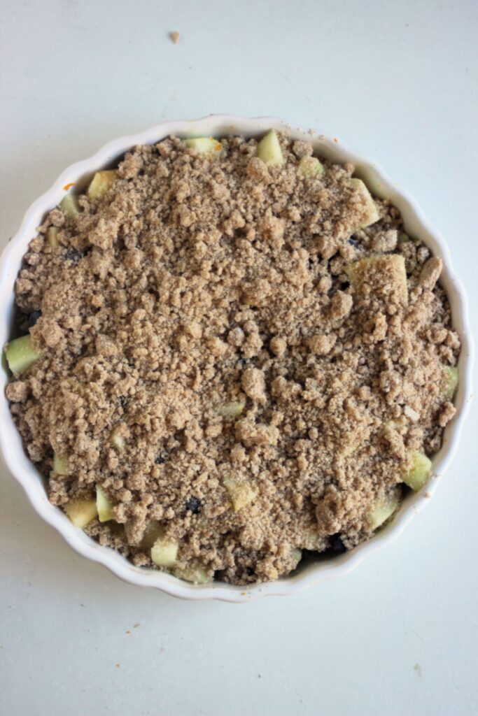 Round white baking dish with apple crumble seen from above.