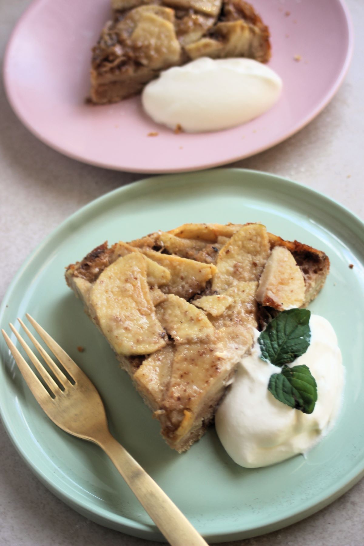 Portion of apple cake with whipped cream and a golden fork on a aqua green plate.