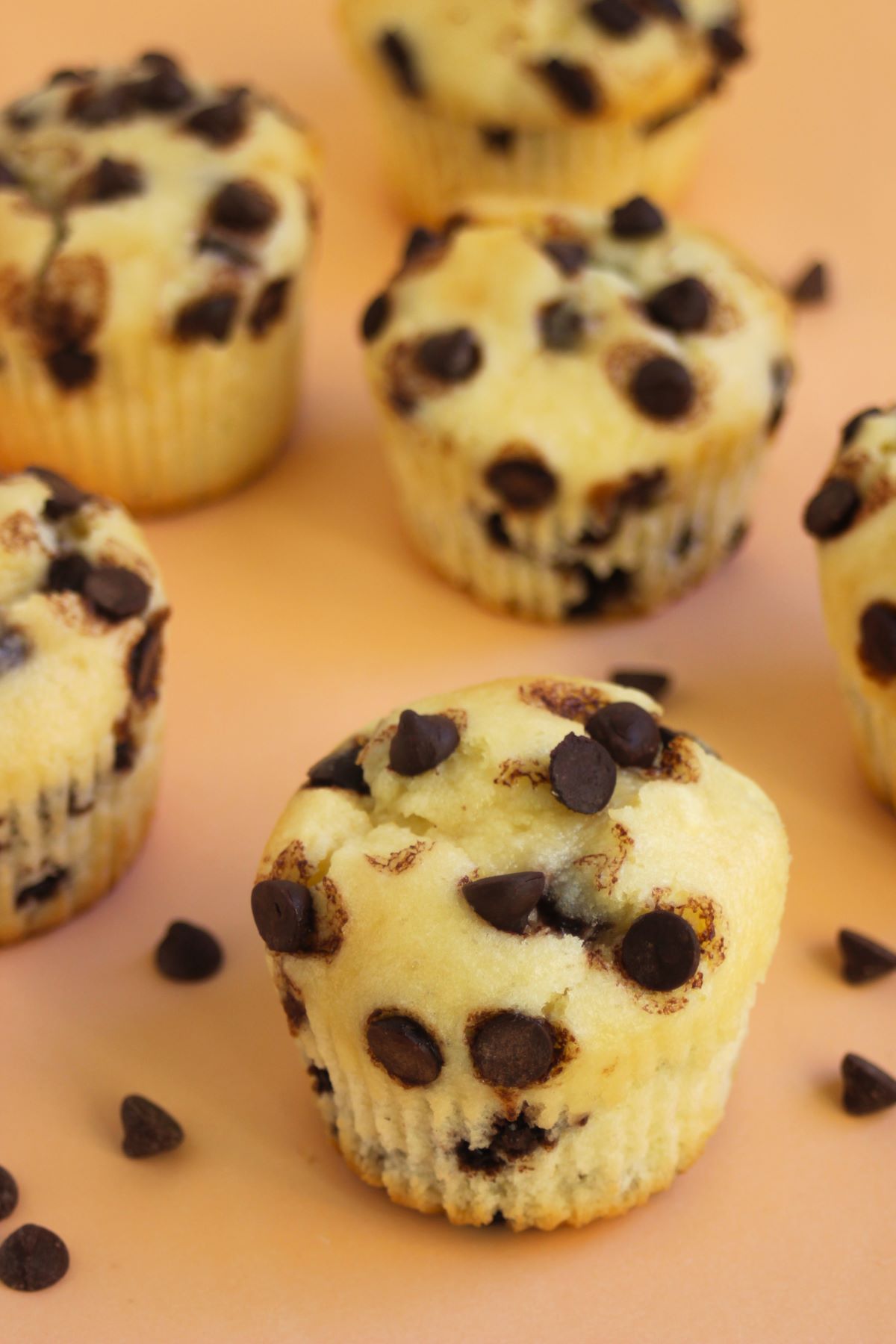 Chocolate chip muffins on a light orange surface,