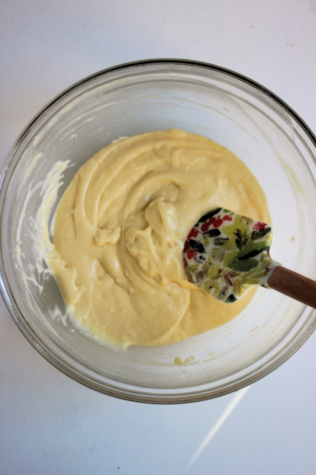 White bowl with a cream colour mixture and a rubber spatula.