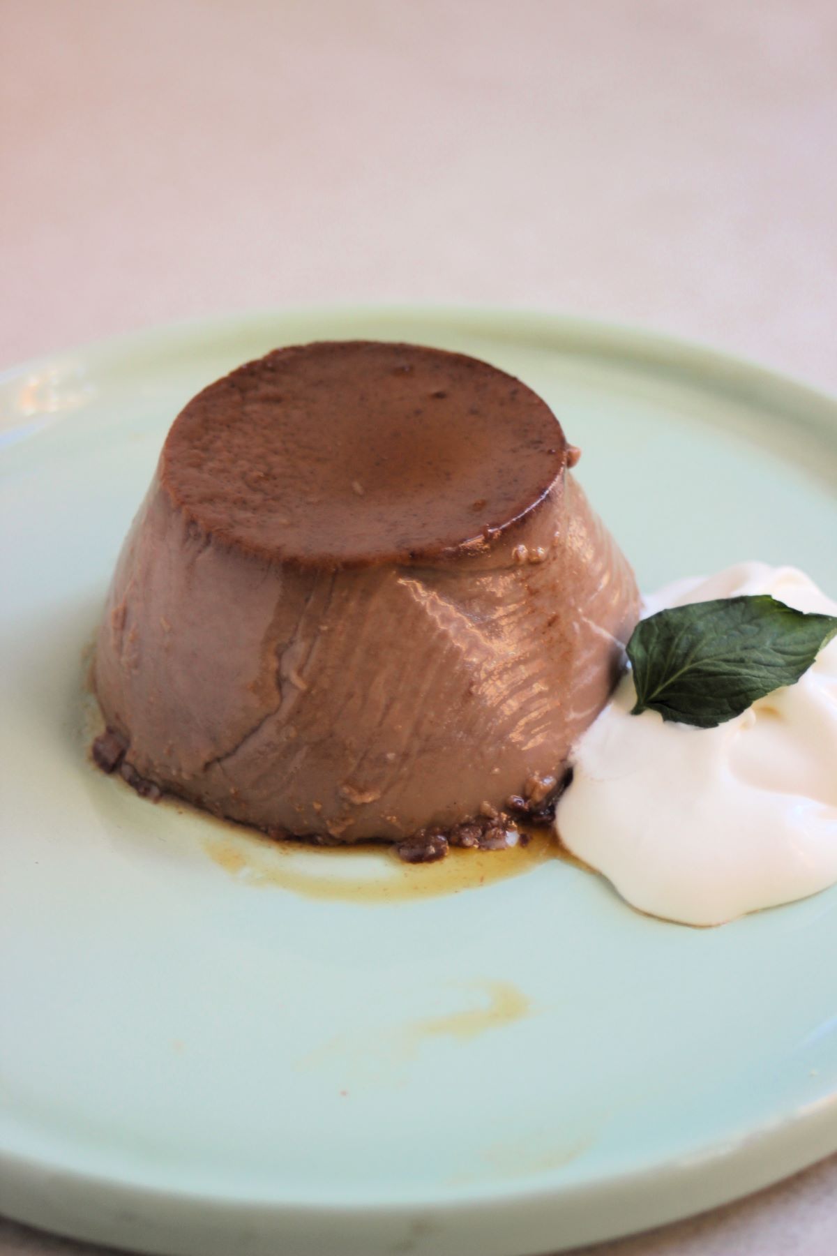 Flan with whipped cream and a mint leaf on an aqua-green plate.