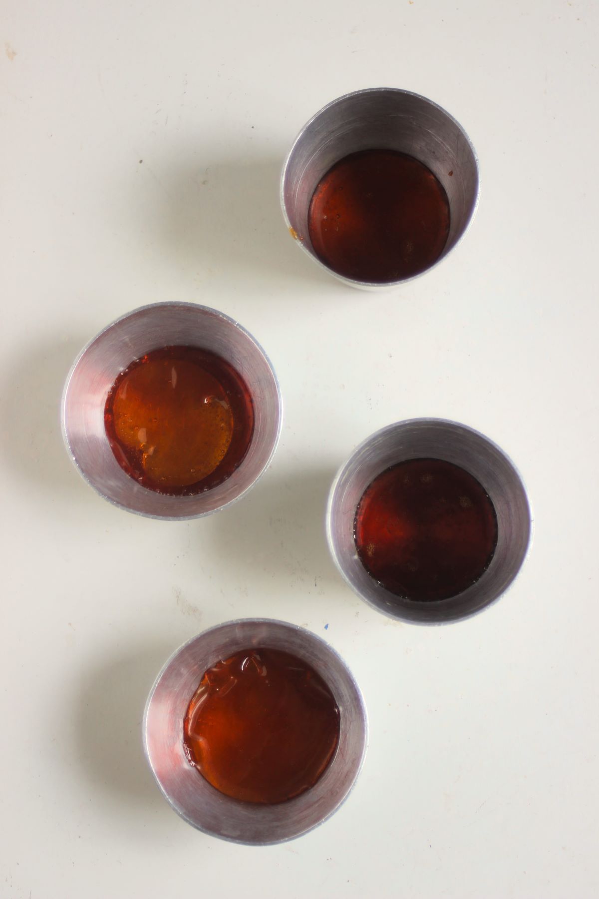 Four individual flan molds with caramel on the background on a white surface seen from above.