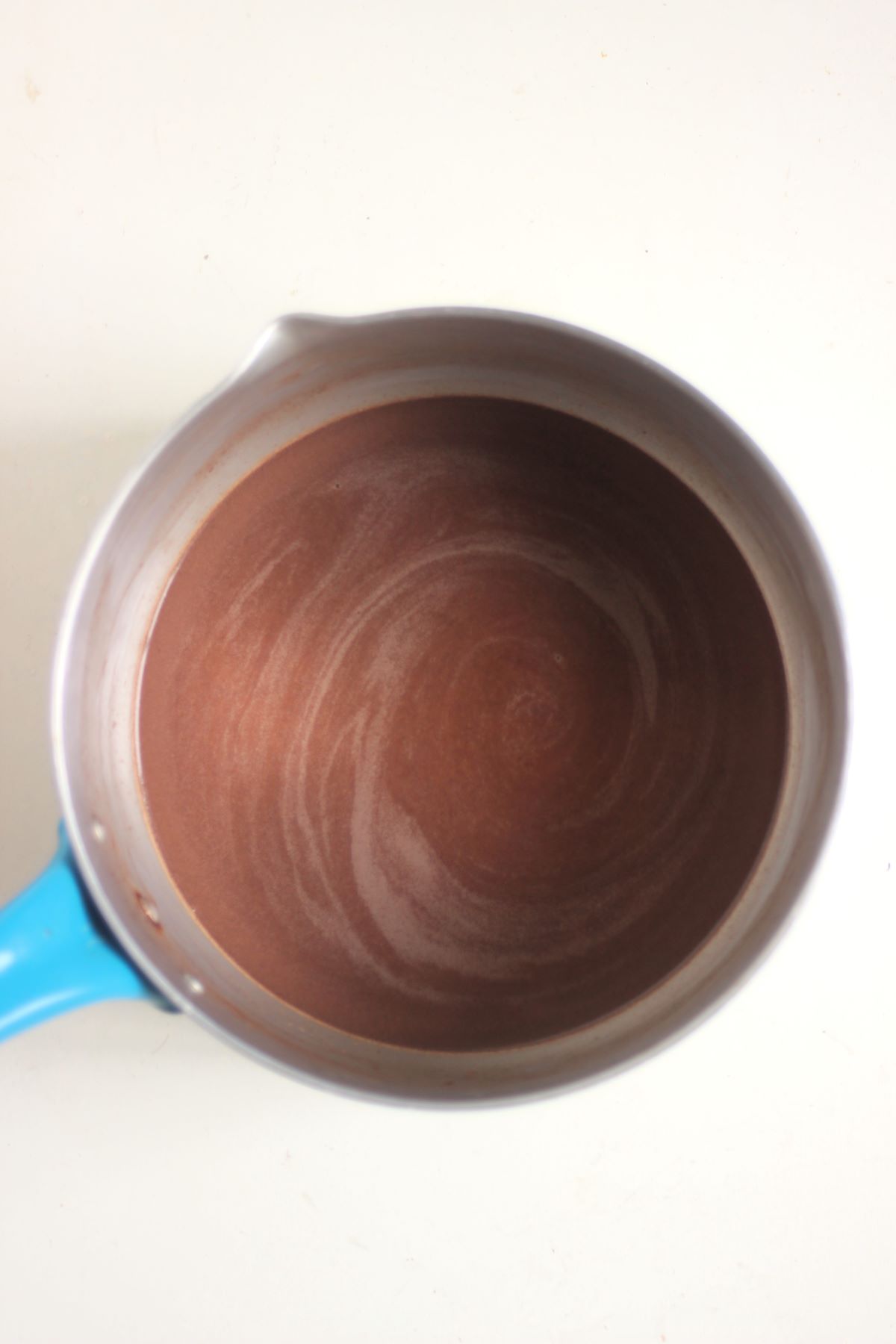 Deep saucepan with a liquid chocolate mixture seen from above. White surface.