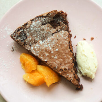 Portion of chocolate cake with orange slices and whipped cream on a pink plate.