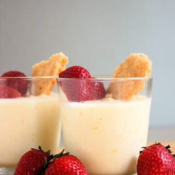 Glass cup with lemon posset, strawberries, and shortcake cookie. Strawberries on the side.