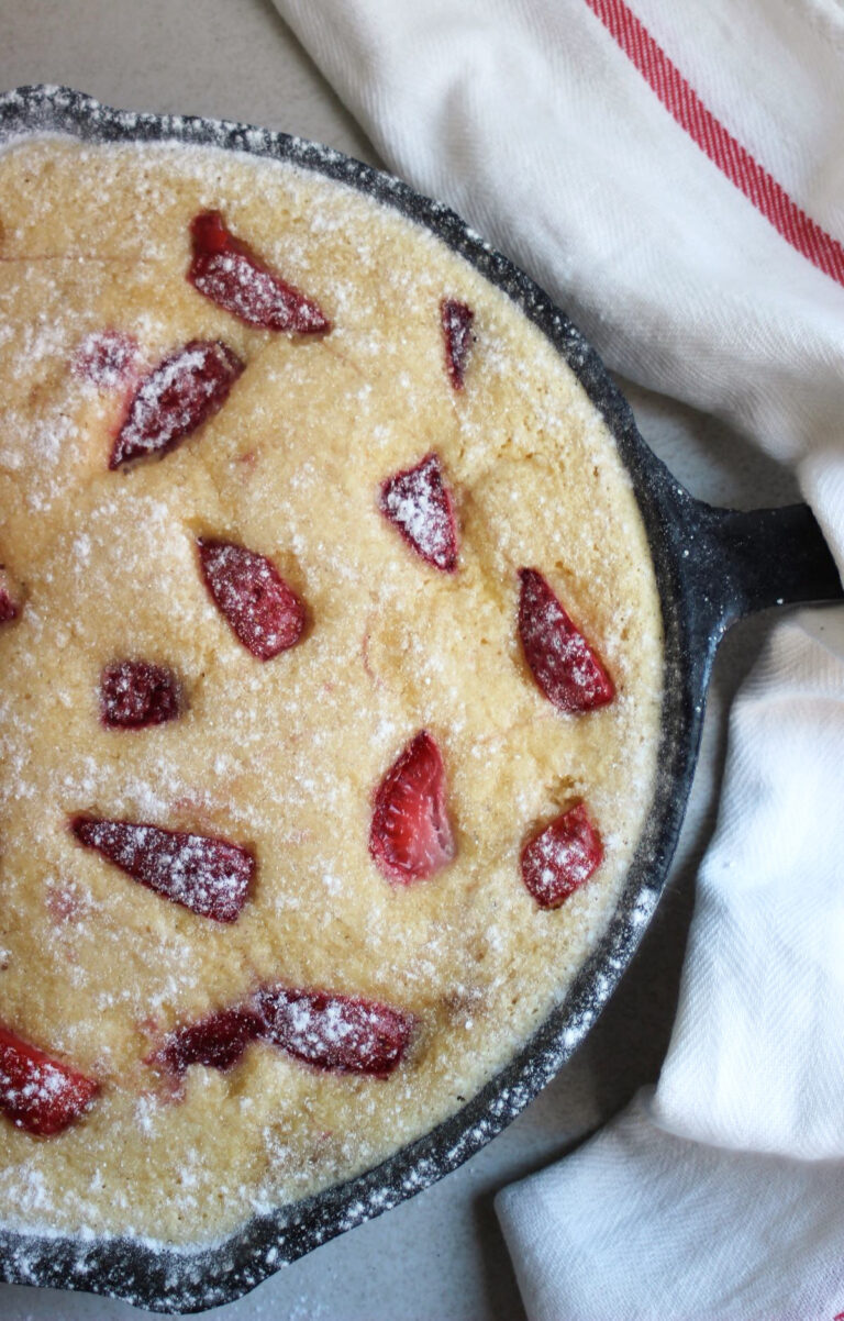 Strawberry clafoutis in a black skillet and a white napkin seen from above.