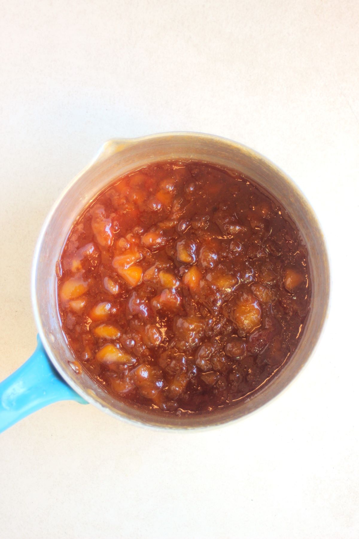 Deep pan with peach marmalade and peach small pieces on a white surface seen from above.