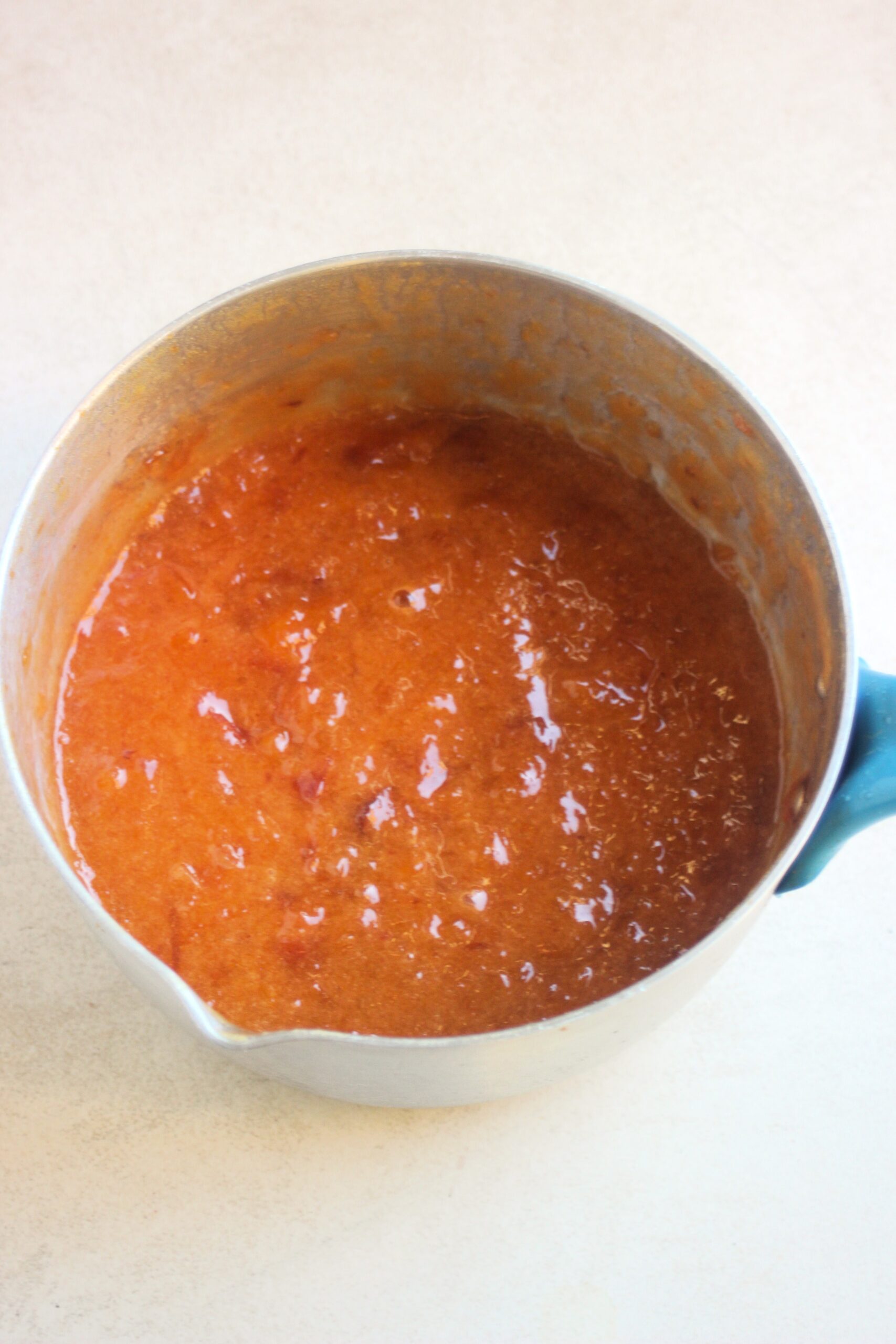 Deep pan with peach marmalade on a white surface.