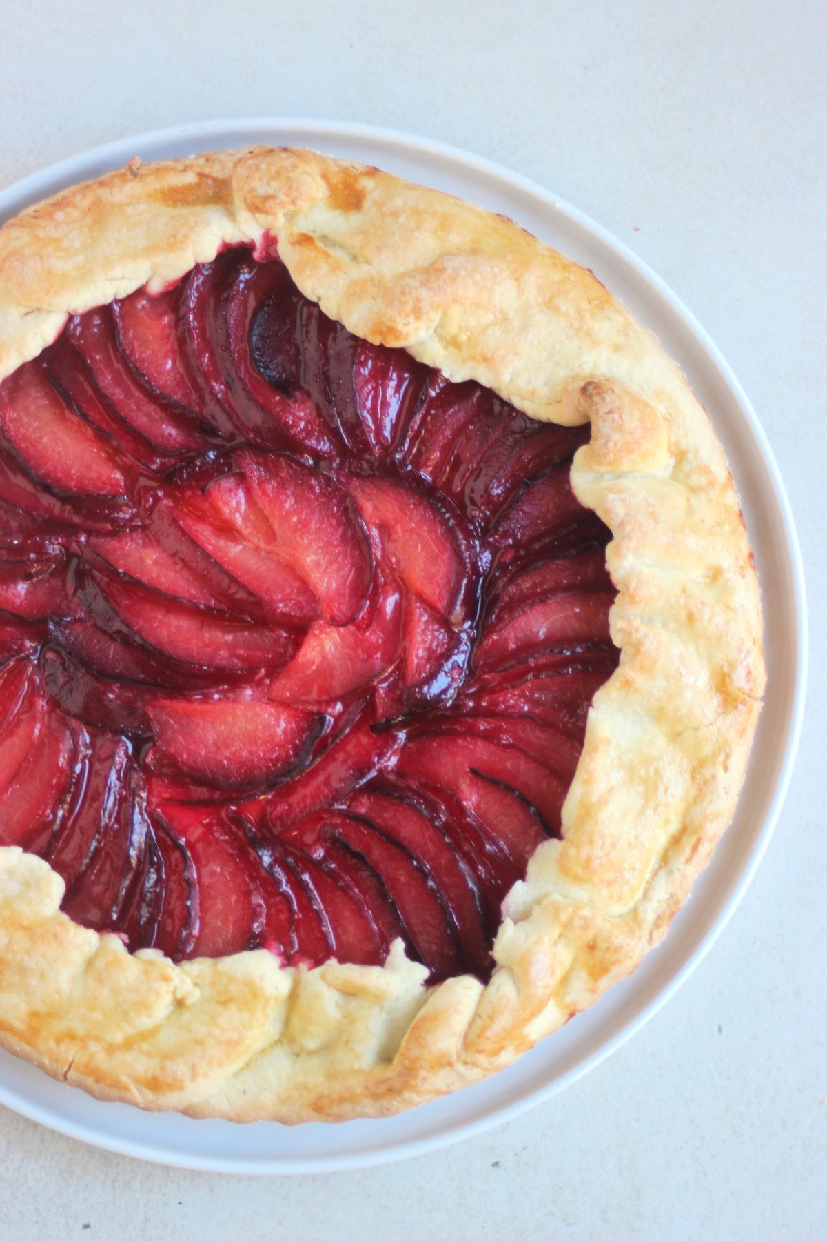 Plum tart on a white plate on a white surface seen from above.