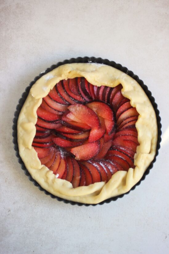 Plum tart in a round baking pie pan on a white surface seen from above