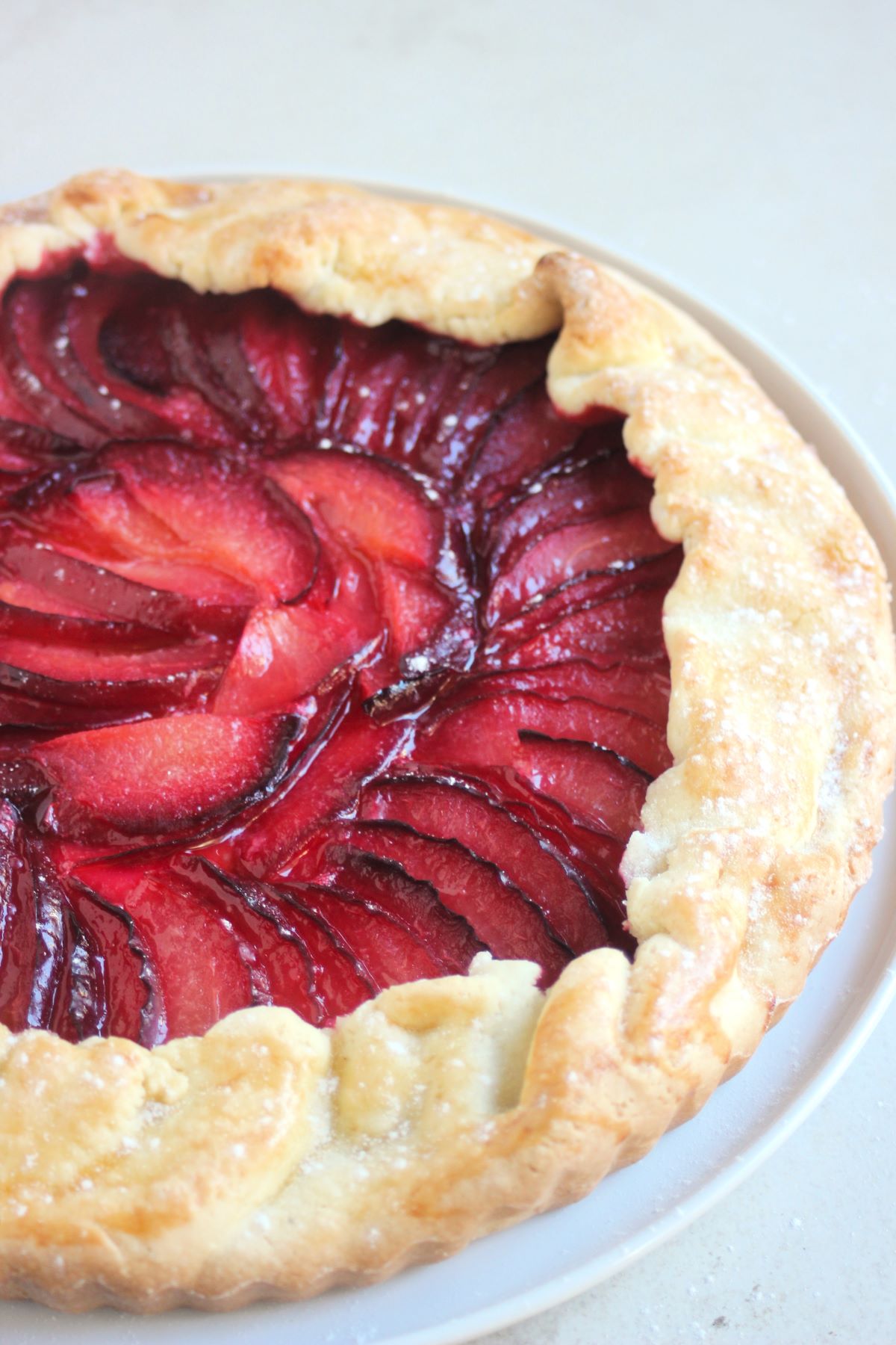 Plum tart on a white plate on a white surface.