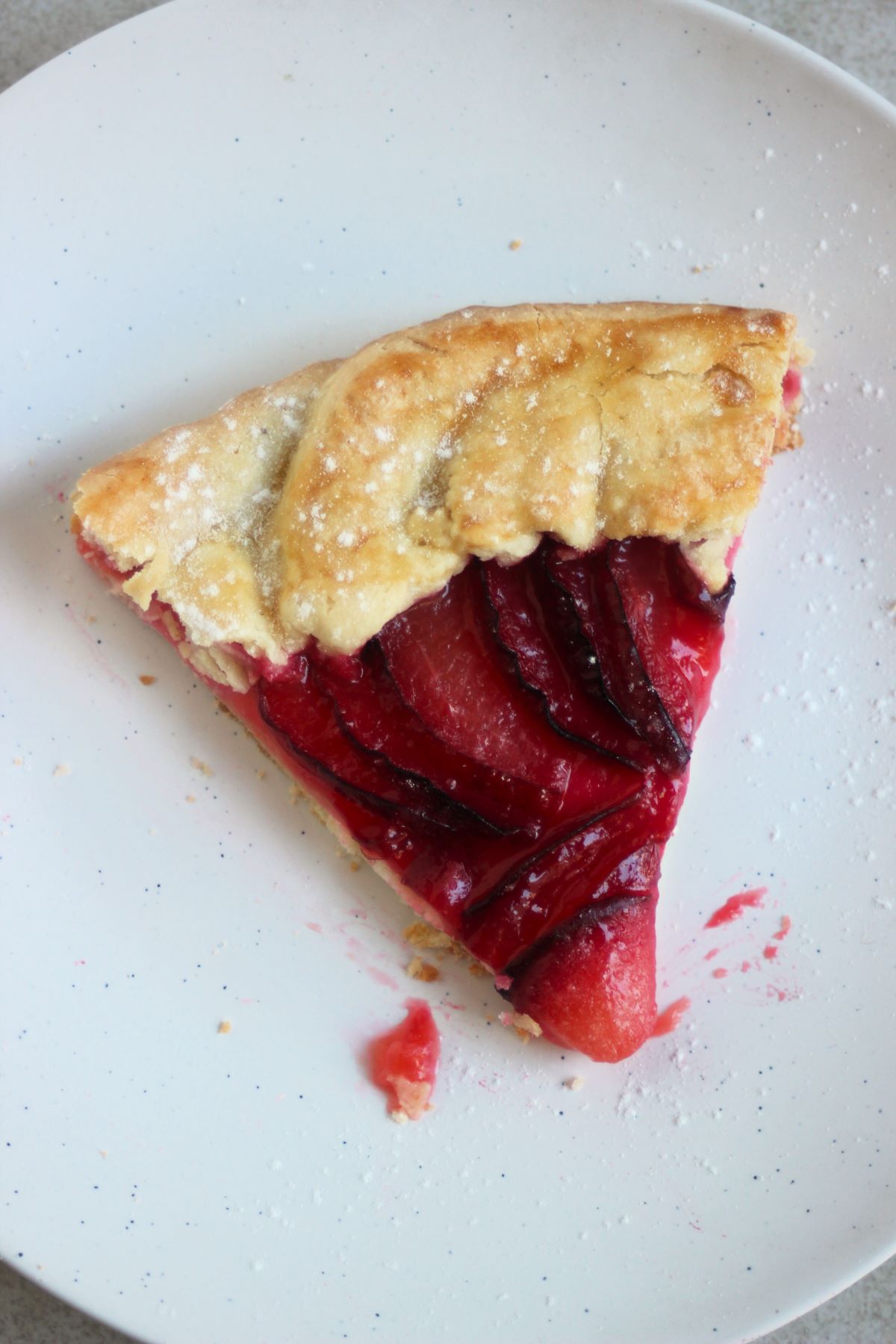 Portion of plum tart on an aqua-green plate seen from above.