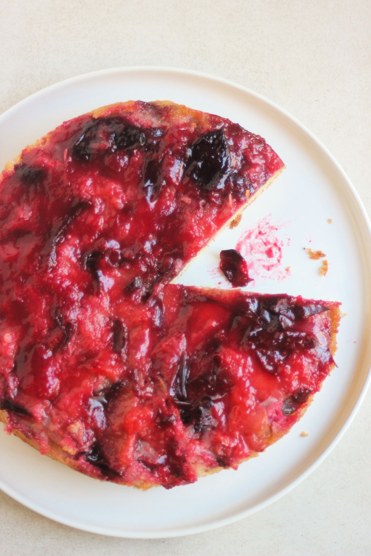 Plum upside down cake without a portion on a white plate seen from above.