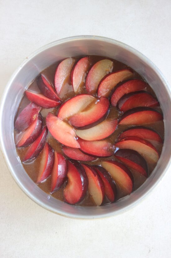 Round cake pan with plum slices arranged in a circle.