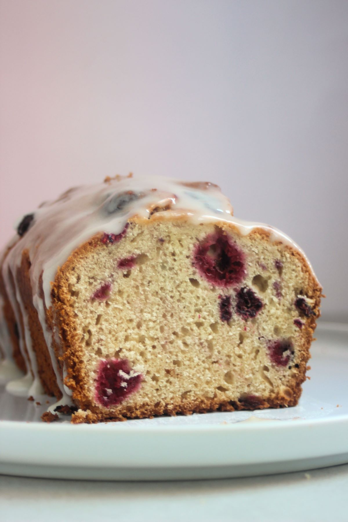 Front view of the inside of raspberry loaf cake with icing on a white plate. Pink background.