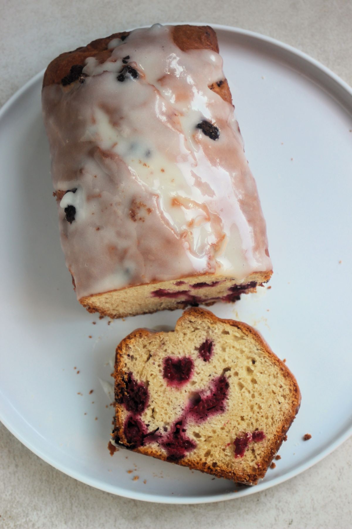 Raspberry loaf cake with icing and a cut portion of it on a white plate seen from above.