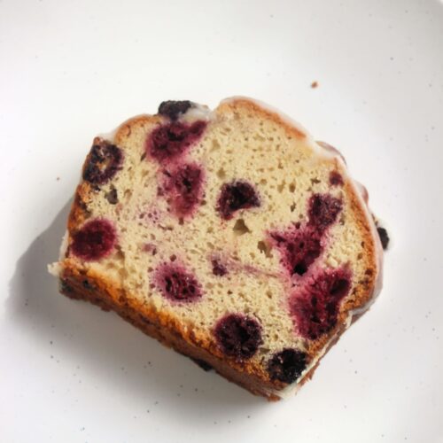 Portion of raspberry loaf cake on a white plate seen from above.