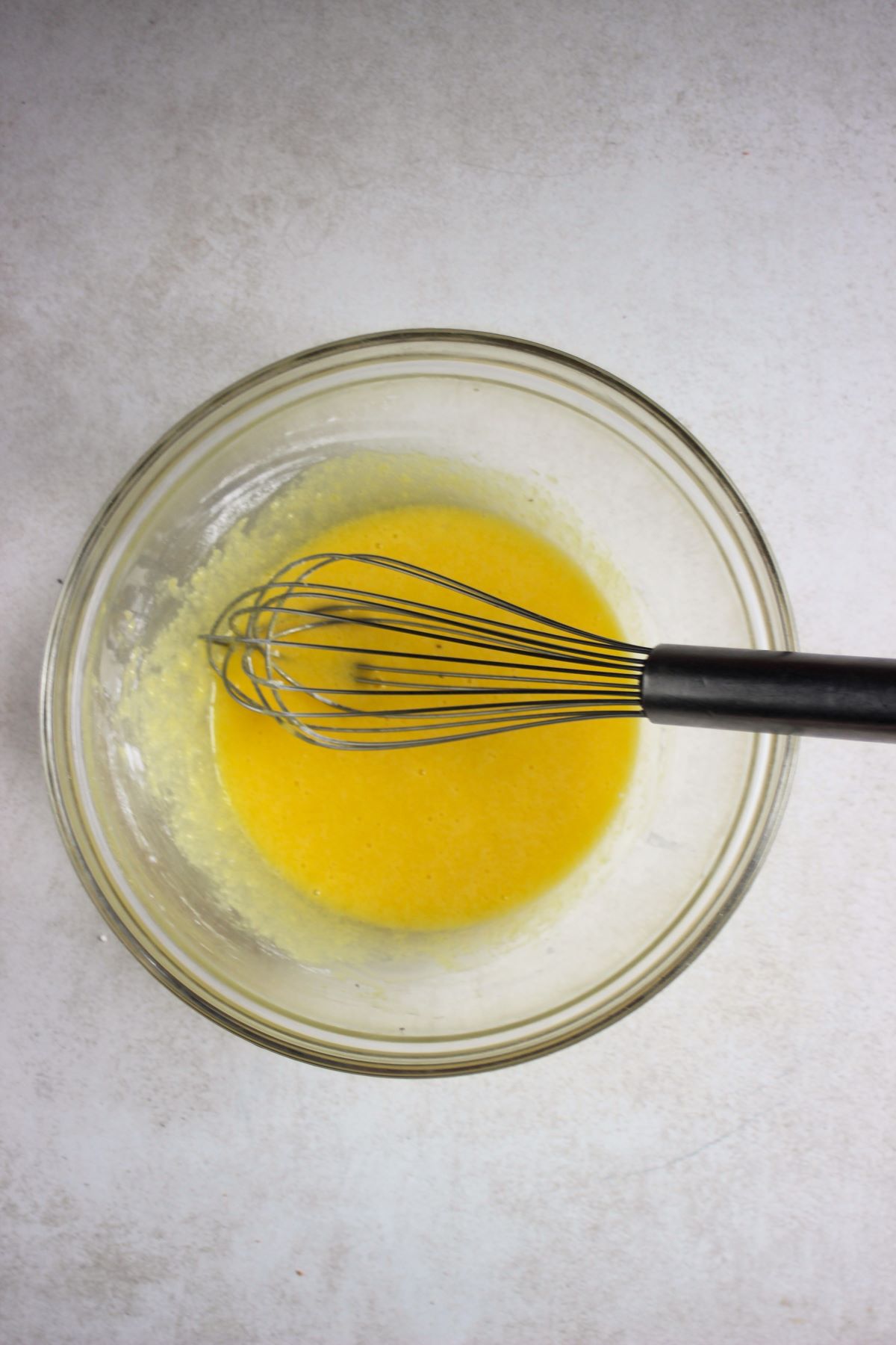 Glass bowl with a yellow mixture and a hand whisk.