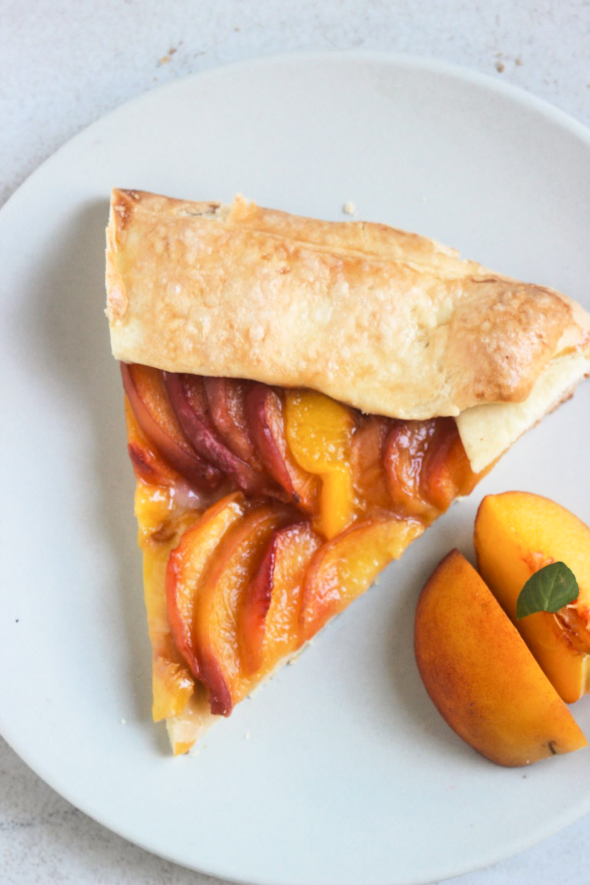 Portion of a peach galette on a white plate and two peach slices on the side.