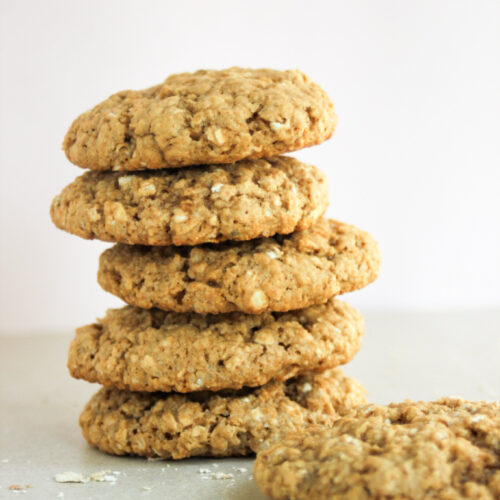 Tower of oat peanut butter cookies and one cookie beside the tower on a white surface.