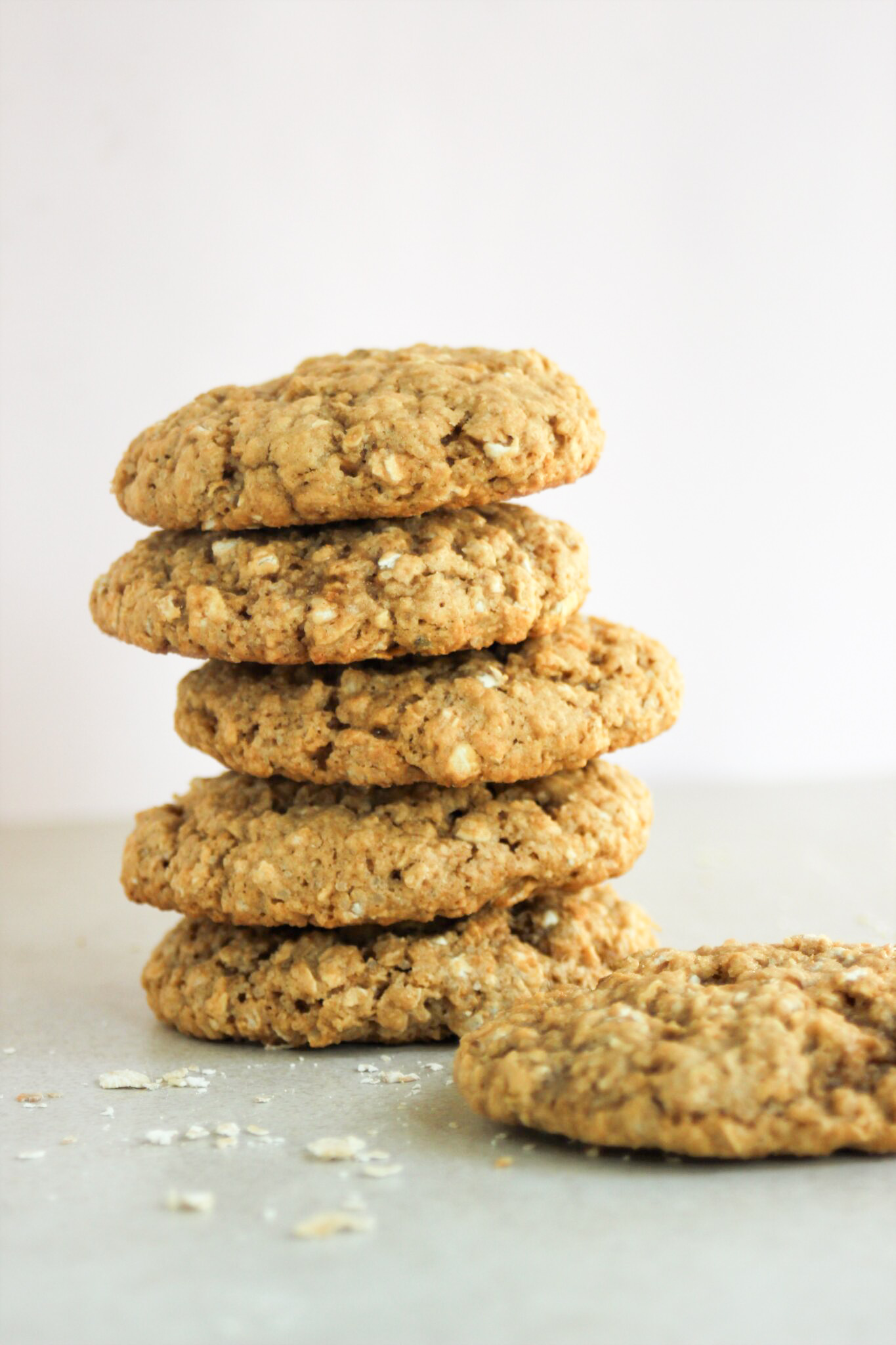 Tower of oat peanut butter cookies and one cookie beside the tower on a white surface.